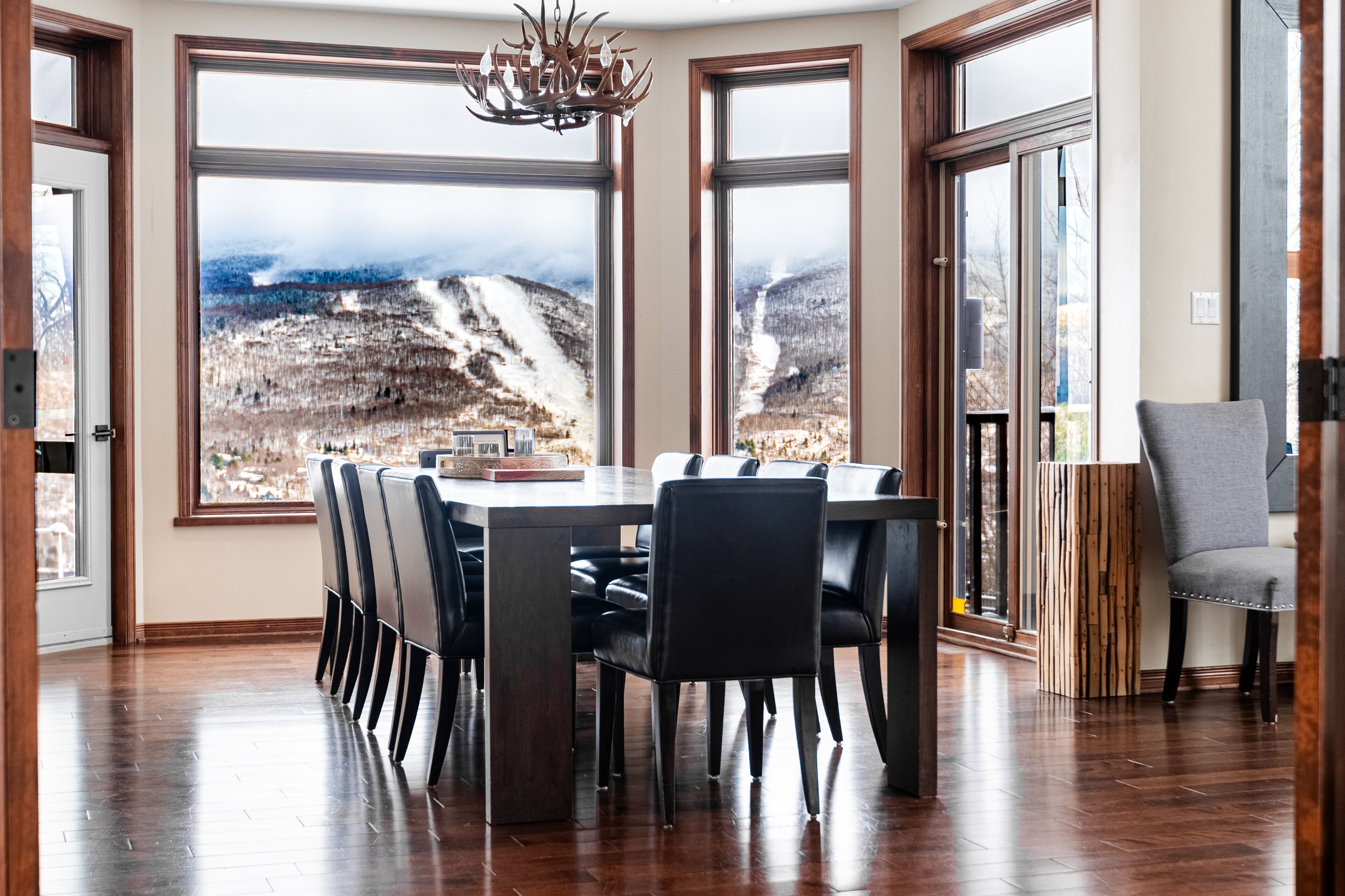 A dining area with a large table and chairs, large windows with a mountain view, and a chandelier.