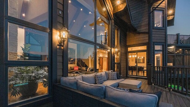 Un espace extérieur moderne, aménagé avec un canapé et des coussins, de grandes fenêtres et une terrasse en bois.