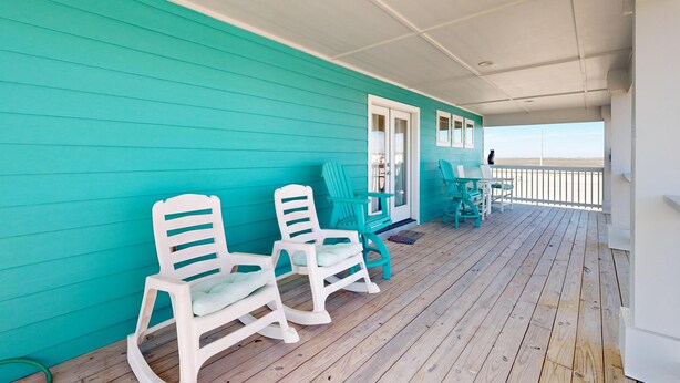 A turquoise deck with white rocking chairs and a table, overlooking a beach. - Luxury Home Detached Suite, Private Pool, Located Near Beach (Port Aransas)