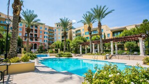 A hotel pool area with a clear blue pool, surrounded by palm trees and a covered seating area. - Escape to Paradise: Luxe 2-Bedroom Retreat (Henderson)