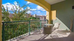 A balcony with a view of buildings and trees, a table with chairs, and a decorative wall piece. - Escape to Paradise: Luxe 2-Bedroom Retreat (Henderson)