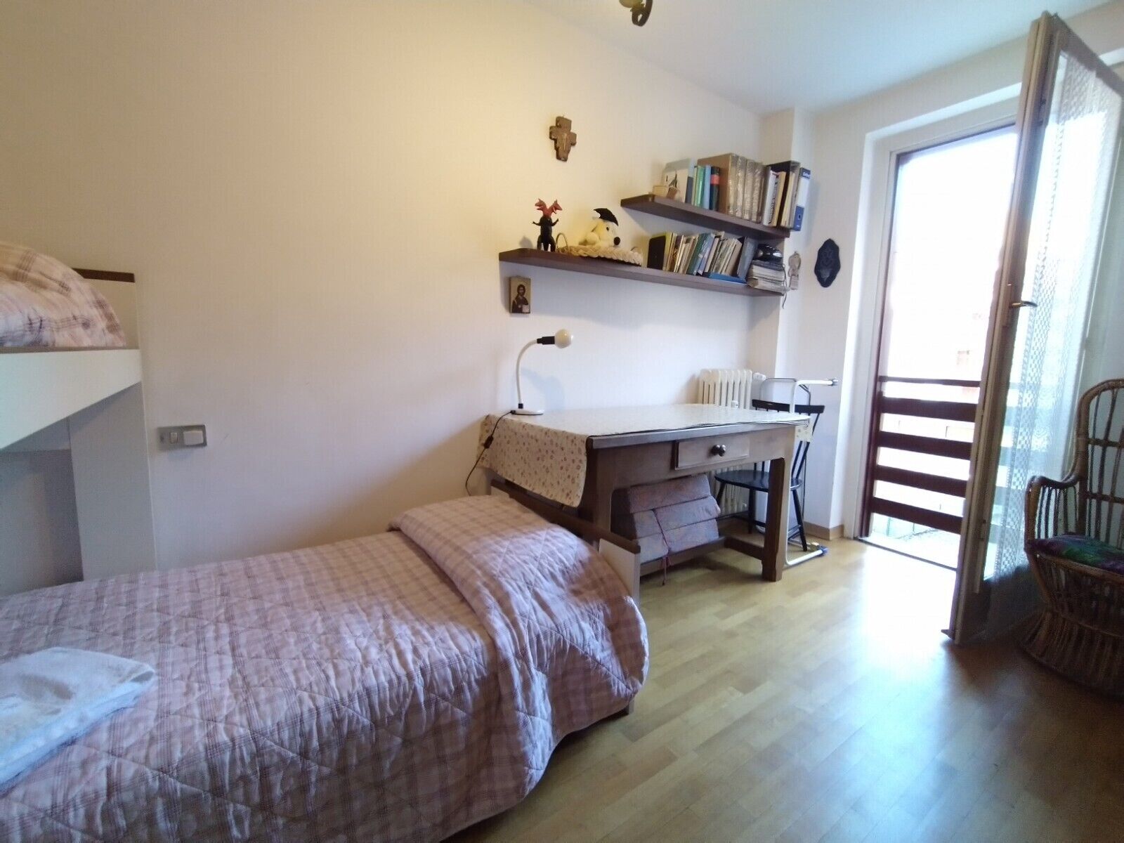 Une chambre avec un lit superposé, un bureau avec une chaise, une bibliothèque et une fenêtre donnant sur un beau paysage.