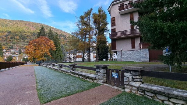 A residential area with a stone wall, a paved path, and a building with balconies. - MEADOWS Apartment (Ponte di Legno)