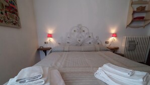 A neatly made bed with a patterned bedspread, two bedside lamps, and a radiator. - MEADOWS Apartment (Ponte di Legno)