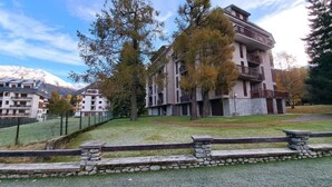 A multi-story building with balconies, surrounded by trees and a grassy area. - MEADOWS Apartment (Ponte di Legno)
