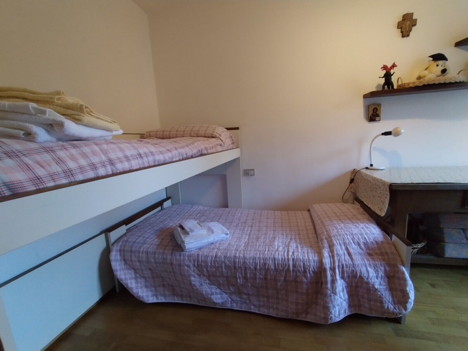 Ein Schlafsaalzimmer mit Etagenbetten, einem Schreibtisch mit Lampe und einem Regal mit Dekoration.