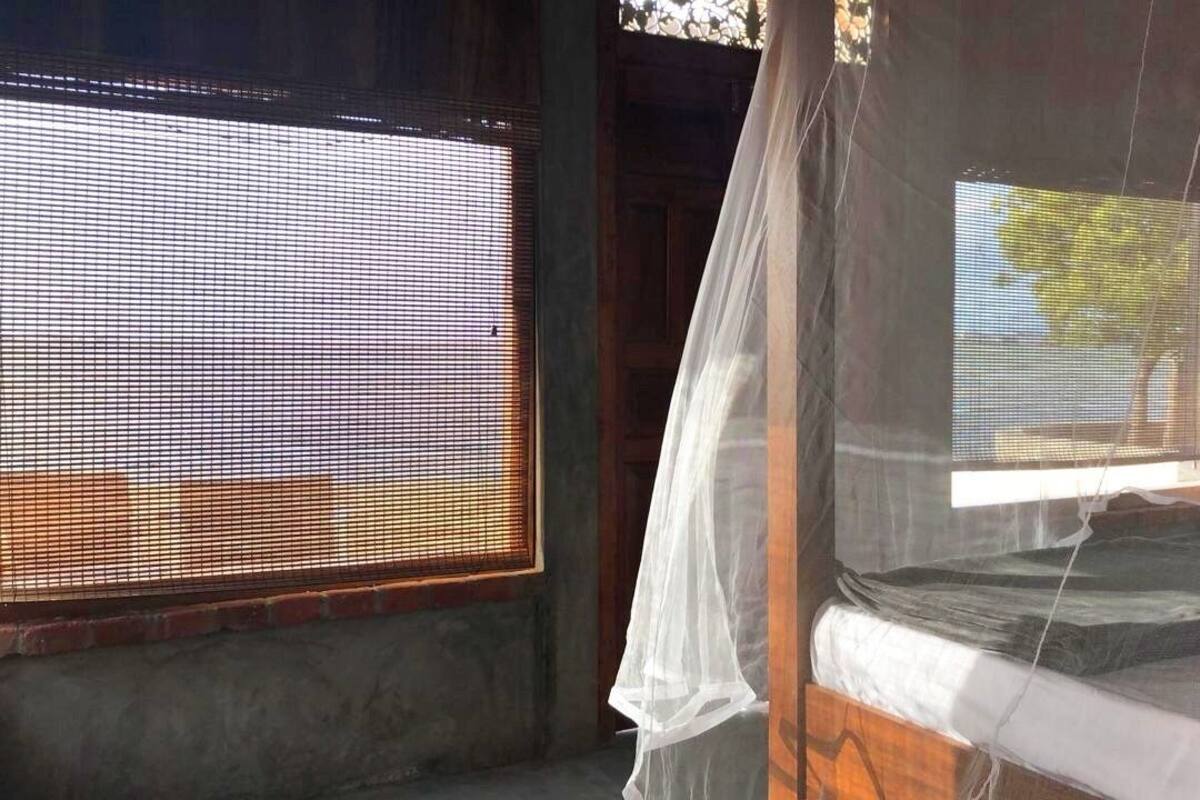 A room with a bed, a window with a mesh screen, and a curtain.
