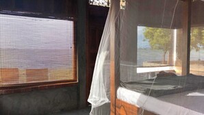 Una habitación con una cama, una ventana con mosquitero y una cortina.