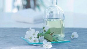 Una botella de vidrio transparente con líquido sobre una superficie azul, con flores blancas y hojas verdes.