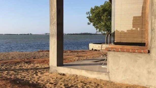 Una estructura de madera frente al mar, con techo de tejas, base de concreto y una ventana con persianas.