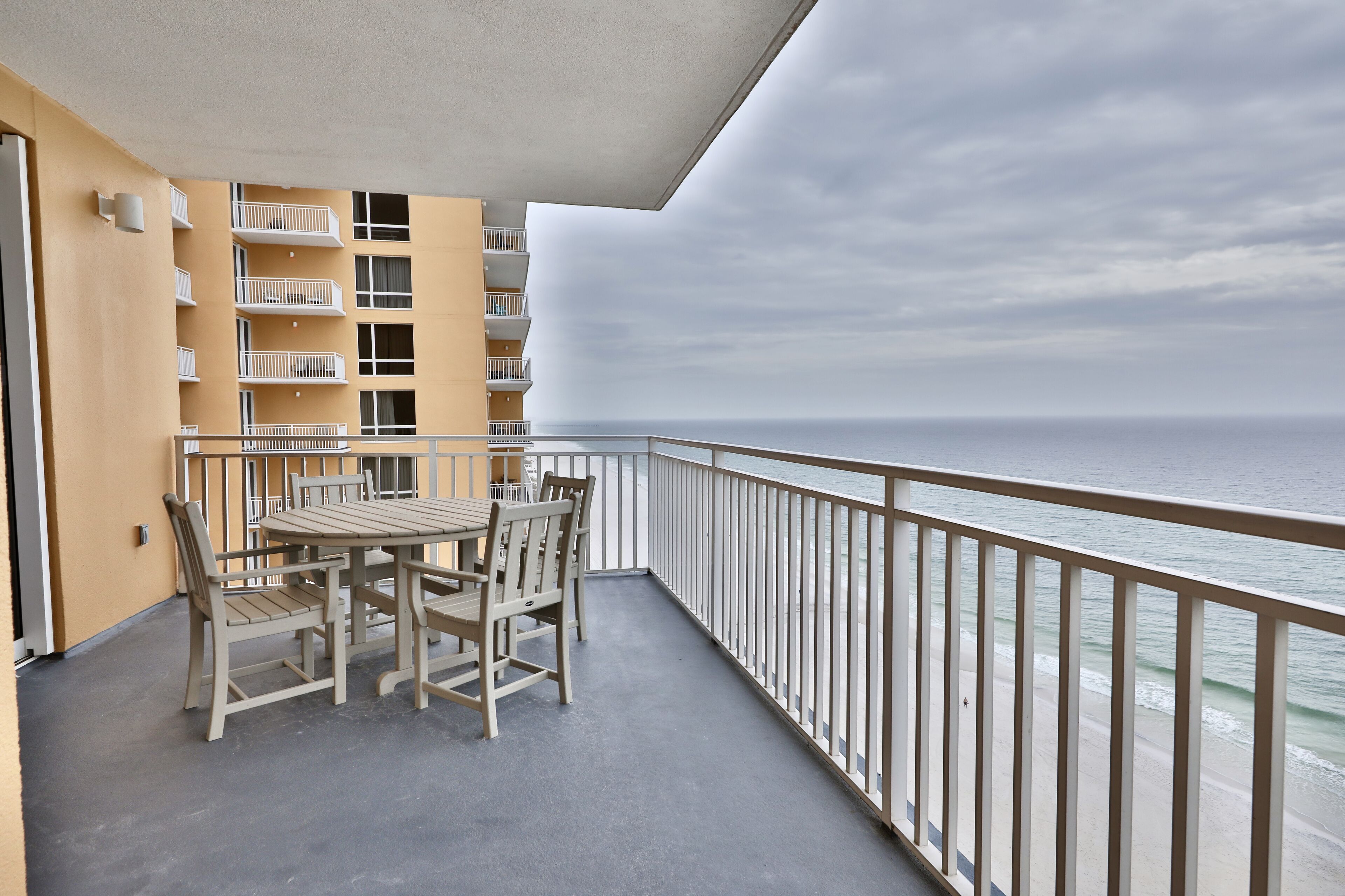 A balcony with a table and chairs, overlooking a beach and ocean.