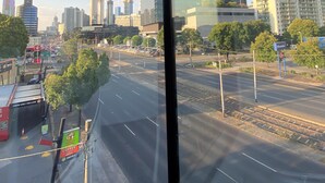 A cityscape through a window with modern buildings, a clear sky, and a road with a coffee shop. - New luxury 3bedroom townhouse cityview (South Melbourne)