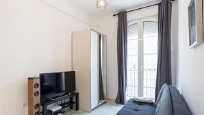 Una sala de estar moderna con un sofá, un televisor sobre un mueble bajo y un ventanal corredero que da a un balcón.