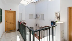 Una habitación con tragaluz, puerta de madera, balcón con barandilla negra y pared blanca con ventana.