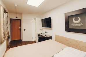 A bedroom with a bed, a desk, a chair, a TV, and a framed picture on the wall. - Berial (Düsseldorf)