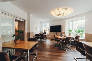 A modern dining area with wooden tables and chairs, a large flat-screen TV, and potted plants. - Berial (Düsseldorf)