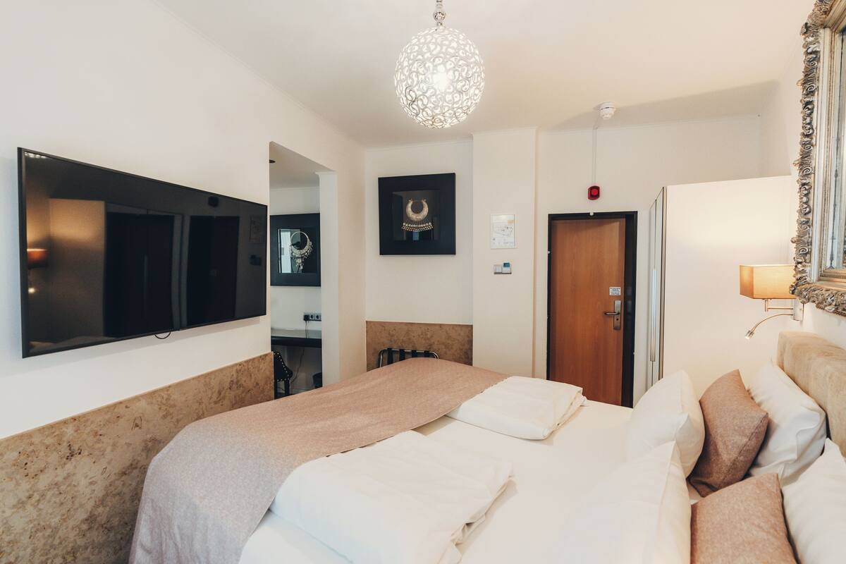 A hotel room with a large bed, a television mounted on the wall, a chandelier, and a framed picture on the wall.