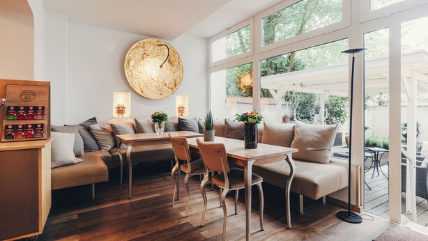 Un interior moderno con una mesa de comedor de madera, asientos acolchados y grandes ventanales con vistas al exterior.