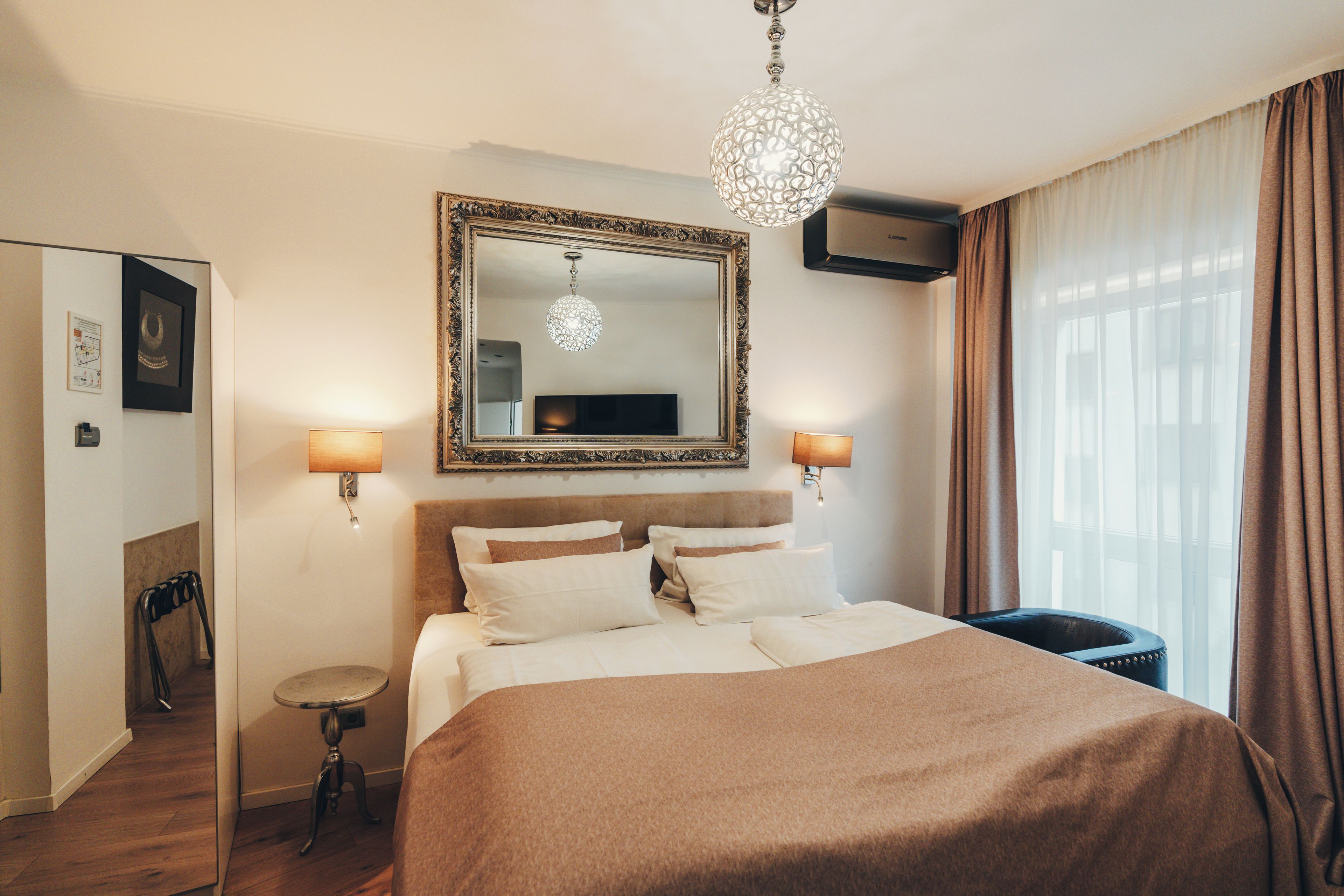 Ein Hotelzimmer mit einem großen Bett, einem Spiegel, zwei Wandlampen und einer Kronleuchter.