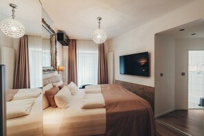 A hotel room with a large bed, two bedside tables, a flat-screen TV mounted on the wall, and a chandelier. - Berial (Düsseldorf)