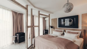Un dormitorio con una cama grande, un cabecero de madera, una lámpara colgante y vistas al exterior a través de cortinas translúcidas.