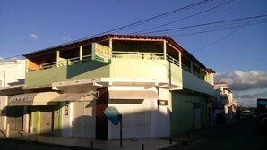 Un edificio de dos plantas con fachada verde y blanca, un balcón en el piso superior y una tienda cerrada en la planta baja.