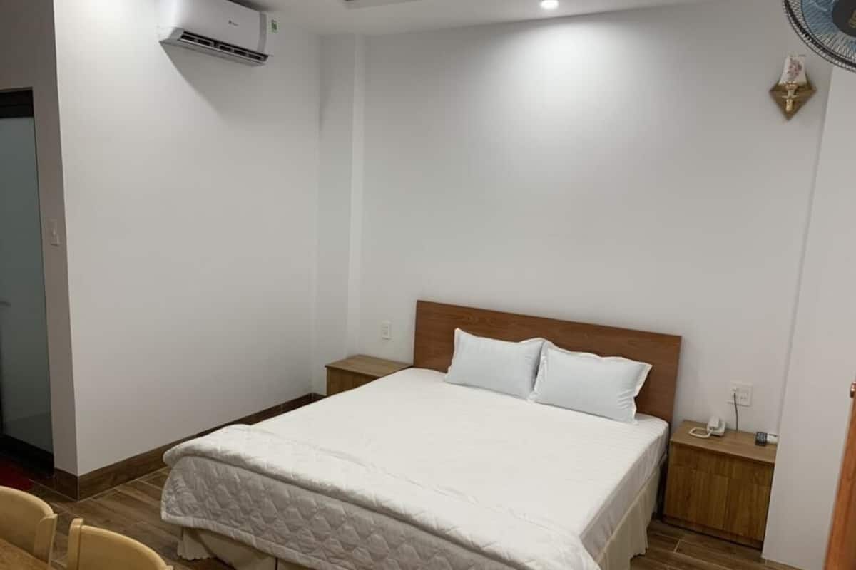 A bedroom with a large bed, a wooden headboard, a bedside table, and a wall-mounted air conditioner.
