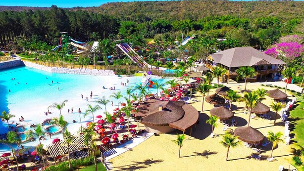 A resort with a large swimming pool, a water park, and a beach area with umbrellas and lounge chairs. - Resort com Desconto Lagoa Thermas Park (Caldas Novas)
