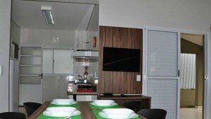 A dining area with a long table set for six, a television mounted on the wall, and a kitchen in the background. - Resort com Desconto Lagoa Thermas Park (Caldas Novas)
