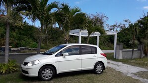 A white car parked on a grassy area with a white gazebo structure in the background. - PARADISE CREEK COTTAGES ON THE BEACH. (Andros Town)