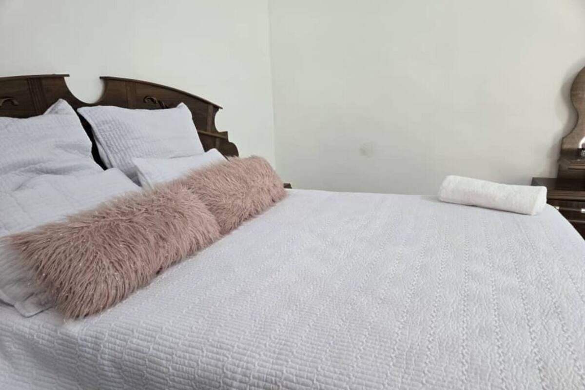 A neatly made bed with a white quilt and a fluffy pink throw.