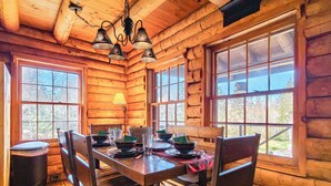 A wooden cabin interior with a dining table set for four, large windows, and a hanging light fixture. - 40 Acre Forested Privacy w/ Deeded Beach Access Near Acadia Schoodic (Prospect Harbor)