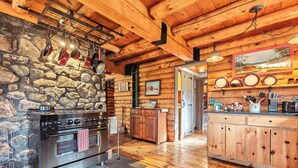A rustic kitchen with a stone wall, wooden beams, and a large stove. - 40 Acre Forested Privacy w/ Deeded Beach Access Near Acadia Schoodic (Prospect Harbor)