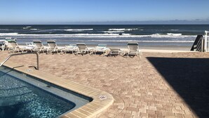 Un área de piscina con sillones de descanso frente al océano, cielo despejado y vista al mar.