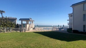 Un área verde con un pabellón, un edificio con balcón y vista a la playa y al océano.