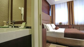 A hotel room with a large bed, a bathroom with a mirror, and a window with curtains.