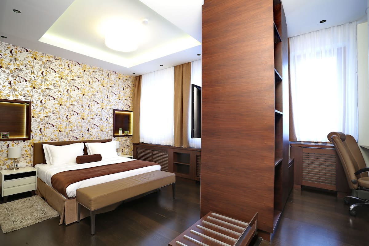 A modern hotel room with a large bed, a flat-screen TV, a wooden desk, and a seating area with a chair.