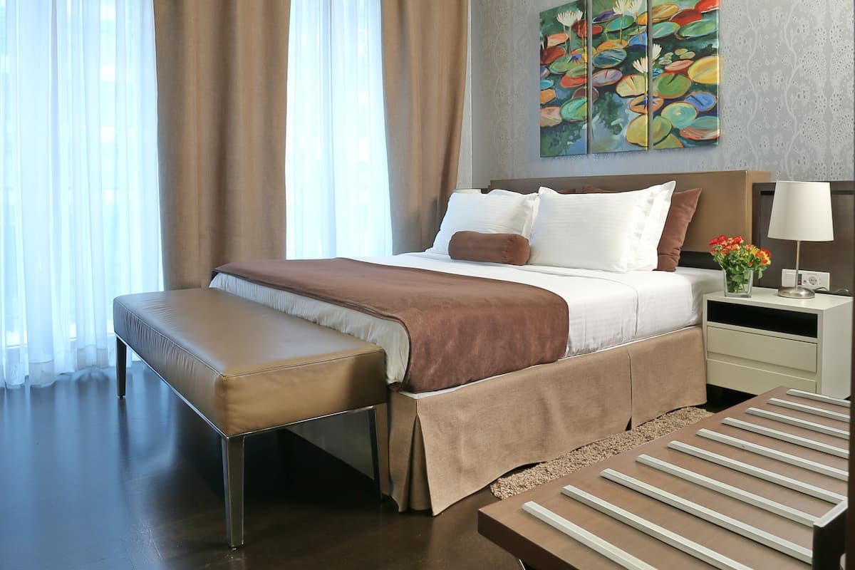 A modern hotel room with a large bed, a bench, a bedside table with a lamp, and a painting on the wall.