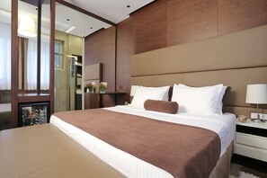 A hotel room with a large bed, a bedside table with a lamp, a mirror, and a minibar.