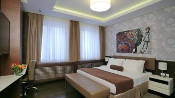 A modern hotel room with a large bed, a bench, a desk, and a painting on the wall.