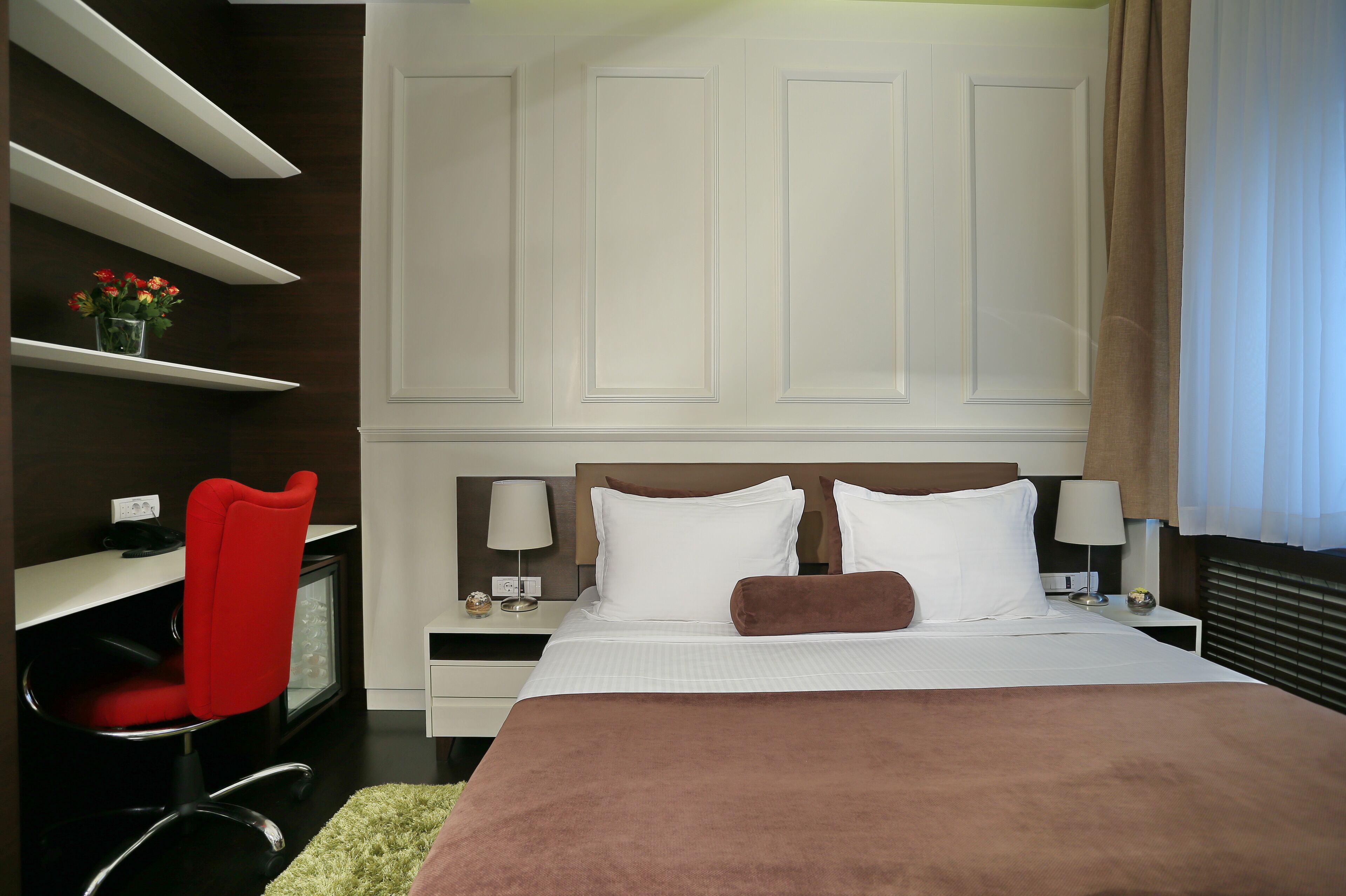 Une chambre d’hôtel avec un grand lit, deux tables de chevet avec des lampes, un fauteuil rouge et un bureau avec un ordinateur.