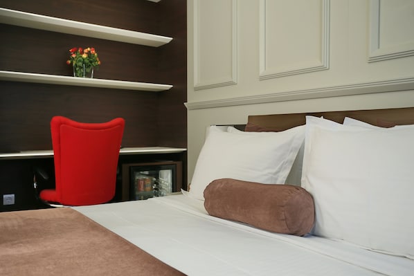 A hotel room with a bed, a red chair, and a shelf with flowers.