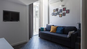A modern living room with a dark grey sofa, a flat-screen TV mounted on the wall, and a series of framed pictures on the wall. - Manuela Apartments Piazza San Domenico in the historic center (Napoli)