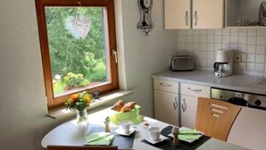 A small kitchen with a dining table, chairs, a window with a view of greenery, and basic kitchen appliances. - Cozy apartment in a rural idyll (Marienhagen)