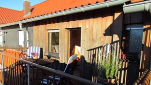 A wooden building with a red roof, a balcony with chairs, and a potted plant. - Cozy apartment in a rural idyll (Marienhagen)