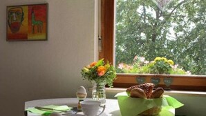 A breakfast table with a vase of flowers, a plate of pastries, and a window with a view of trees. - Cozy apartment in a rural idyll (Marienhagen)