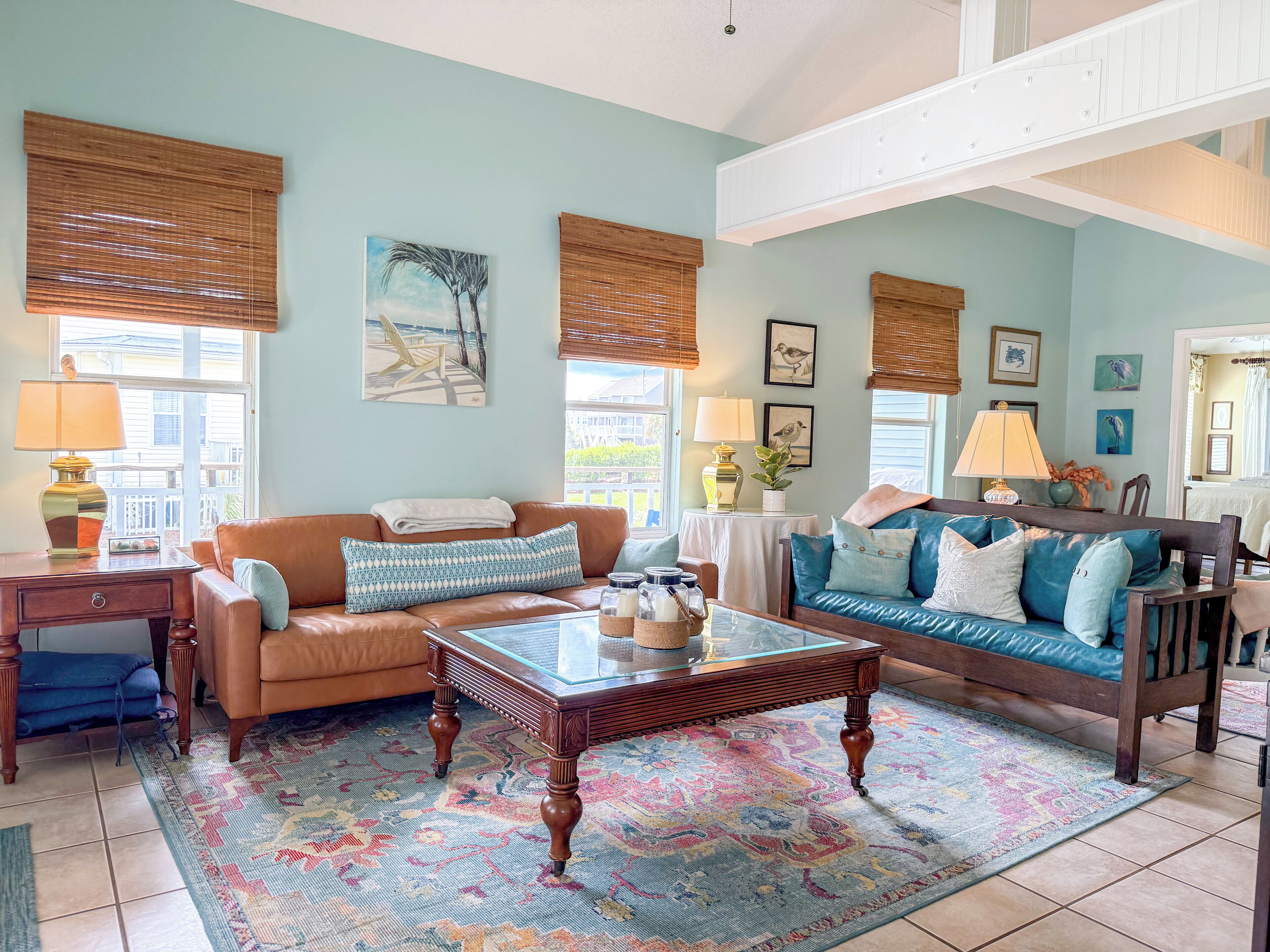 A living room with a brown leather sofa, a blue sofa, a glass coffee table, and a patterned rug.