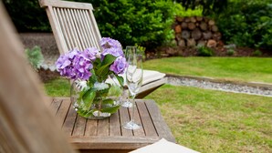 Ein Holztisch mit einer Glasvase, die violette Blumen und zwei Weingläser enthält.