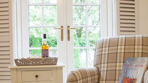 Ein kariierter Sessel mit einem Buch mit dem Titel 'The Scotch Whisky Book' und einer Flasche schottischem Whisky auf einem kleinen Tisch vor einer weißen Tür mit einem Fenster.
