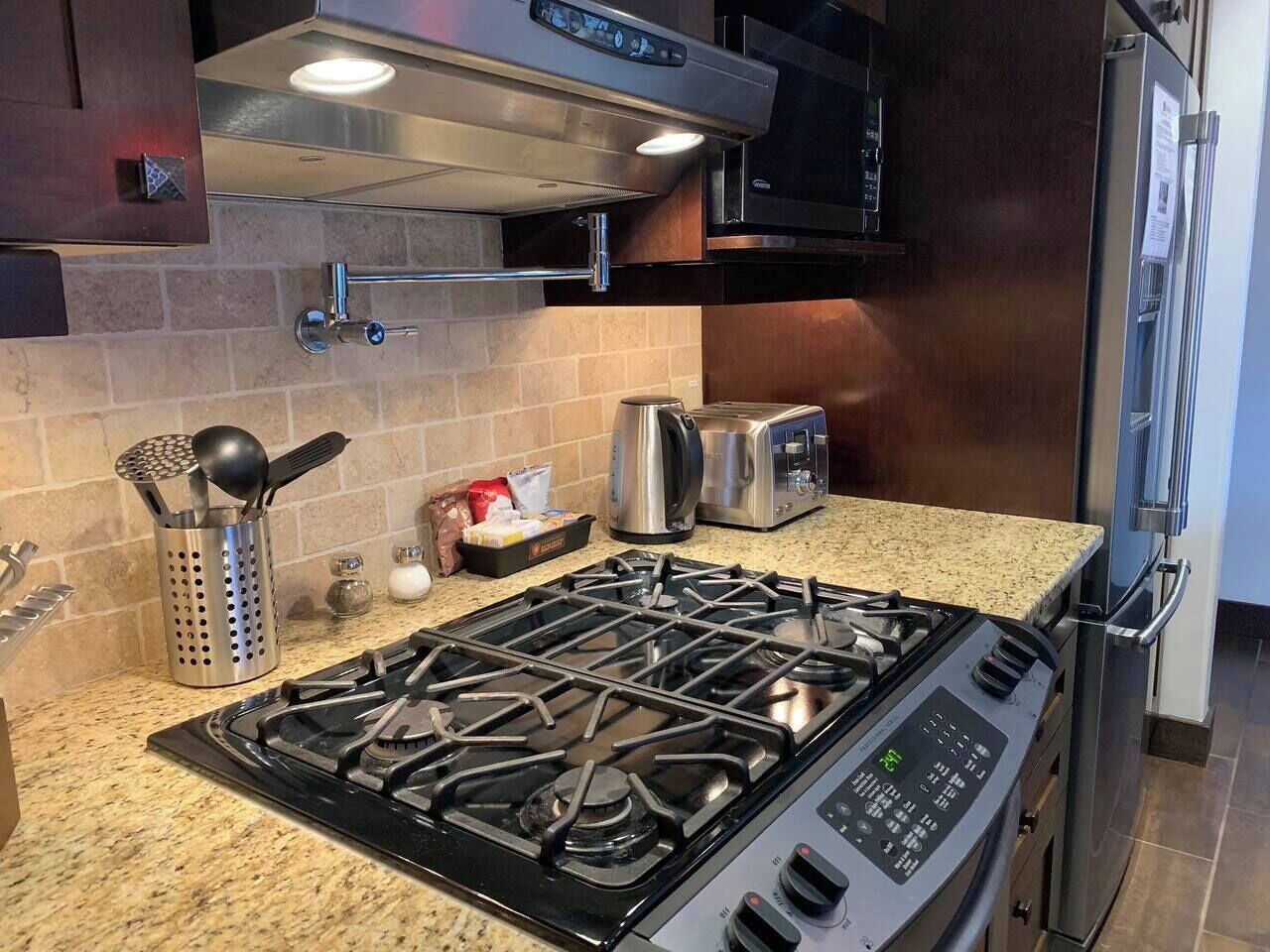 A modern kitchen with a gas stove, stainless steel appliances, and a granite countertop.